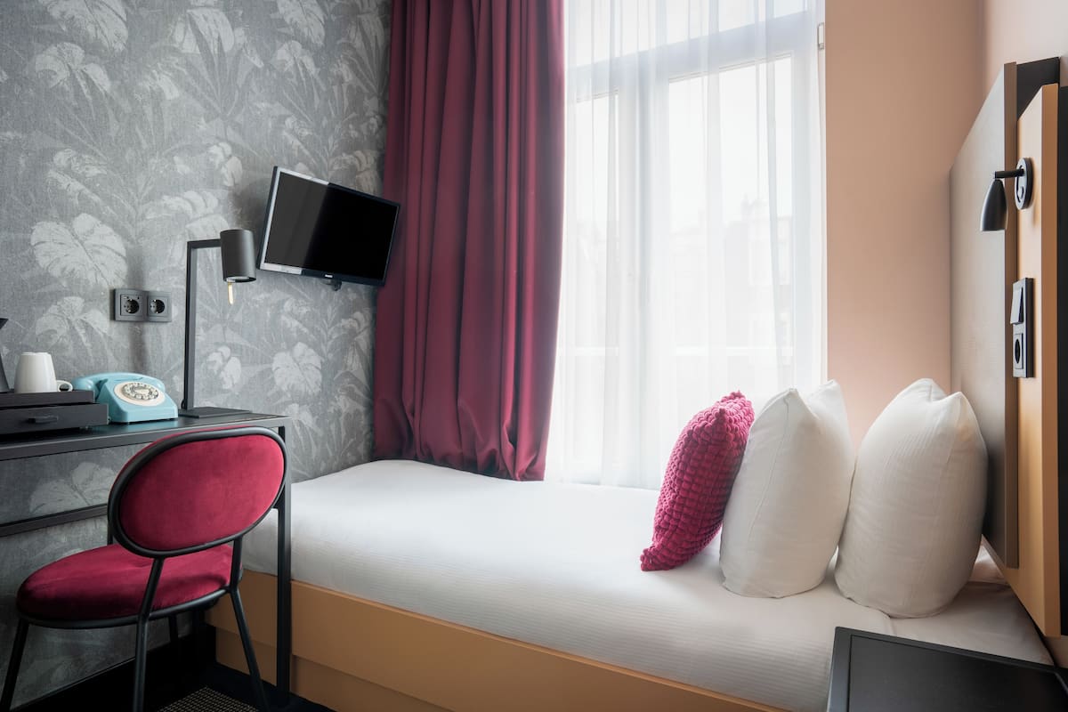 Habitación de hotel con cama, escritorio con computadora y teléfono, una silla y televisor montado en la pared.