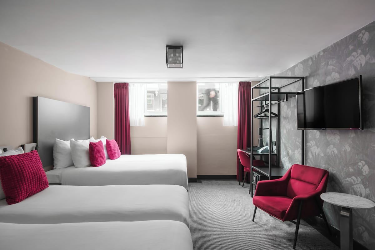 Habitación de hotel con dos camas, una silla roja, un escritorio, un televisor y una ventana con cortinas.