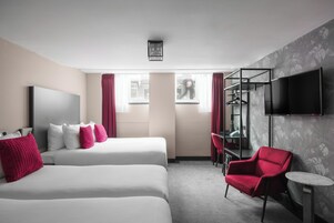 Habitación de hotel con dos camas, una silla roja, un escritorio, un televisor y una ventana con cortinas.