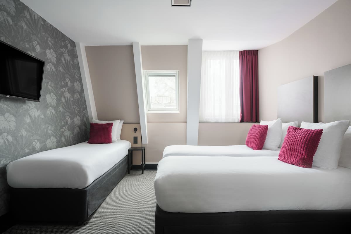 Habitación de hotel con dos camas, un televisor de pantalla plana en la pared, una ventana con cortinas y una mesita.