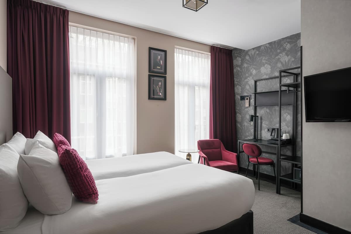 Una habitación de hotel con dos camas, un escritorio, una silla, un televisor y una estantería.