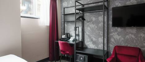 Una habitación de hotel con una cama, un escritorio con una silla, un televisor y un armario.
