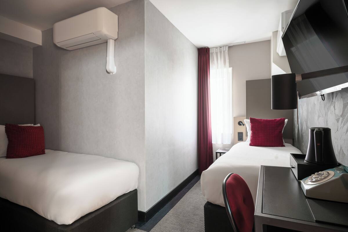 Habitación de hotel con dos camas, un escritorio con silla, un televisor y un equipo de aire acondicionado.