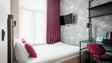 Habitación compacta con cama, escritorio, silla, televisor y ventana con cortinas.