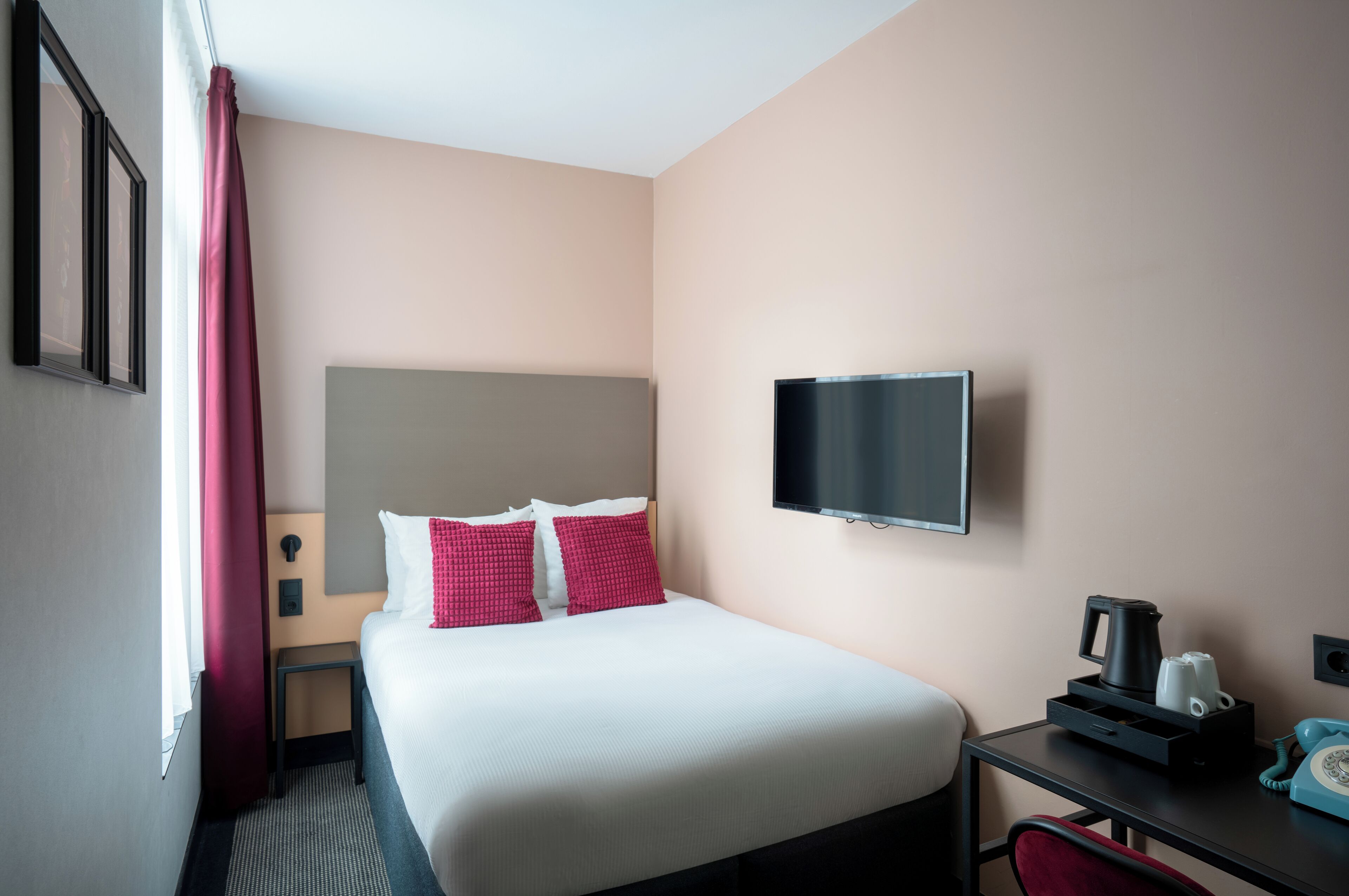 A hotel room with a bed, a TV, a desk with a phone, and a coffee maker.