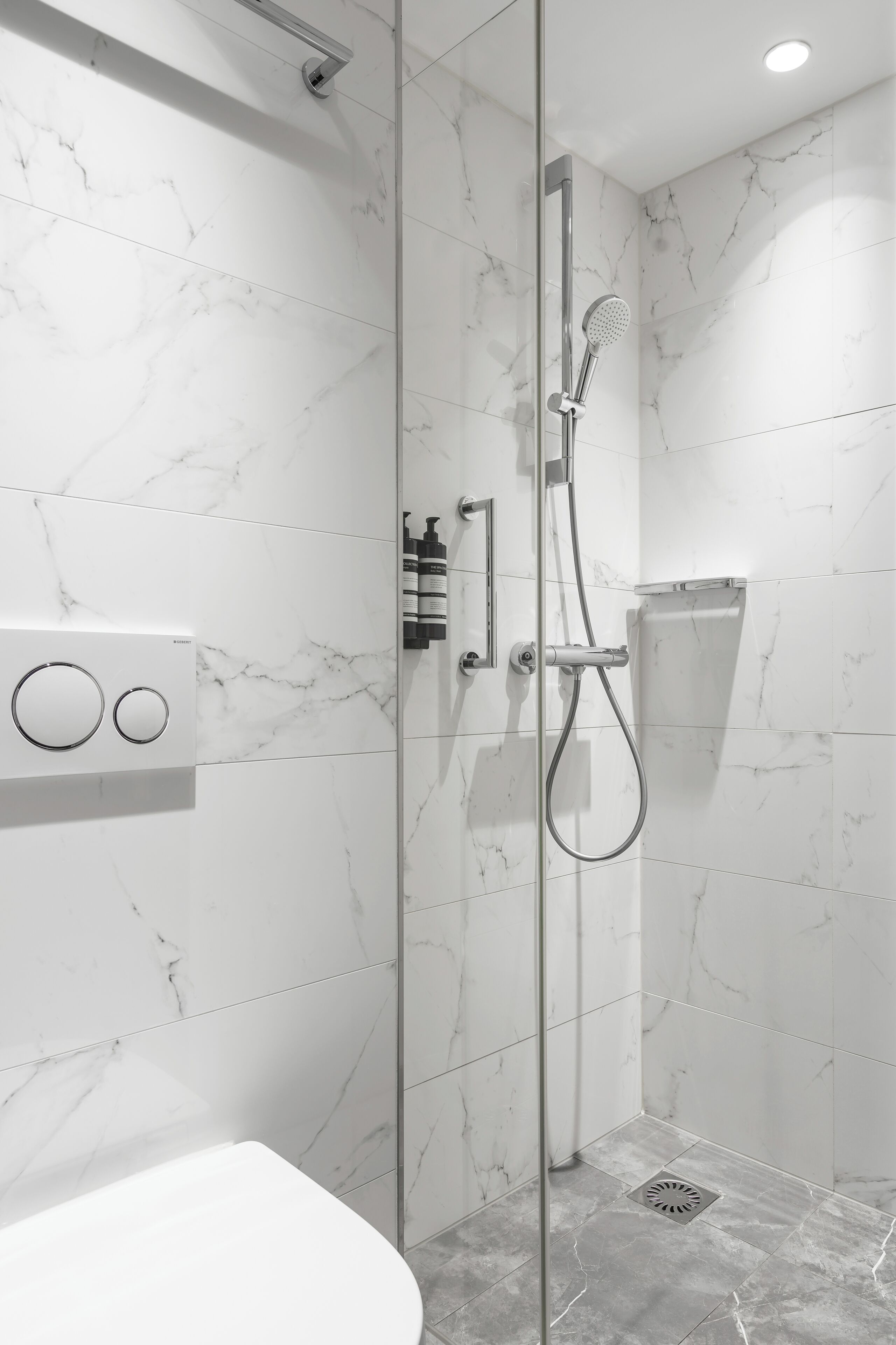 Een moderne badkamer met een douchecabine van glas, marmeren wanden en een ingebouwd toilet.