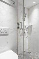 A modern bathroom with a glass-enclosed shower, marble walls, and a built-in toilet.