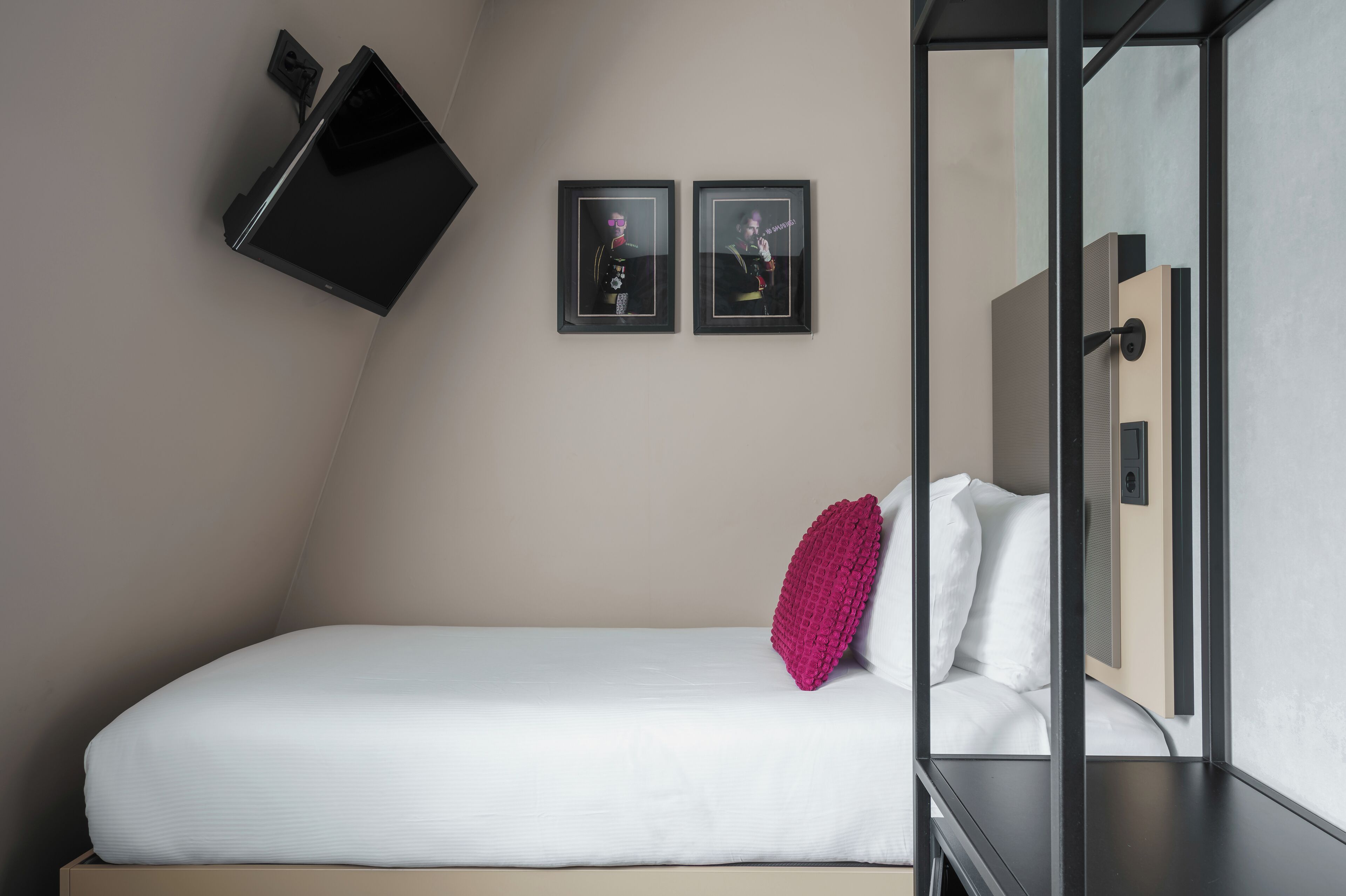 A modern hotel room with a bed, a flat-screen TV mounted on the wall, and two framed pictures.
