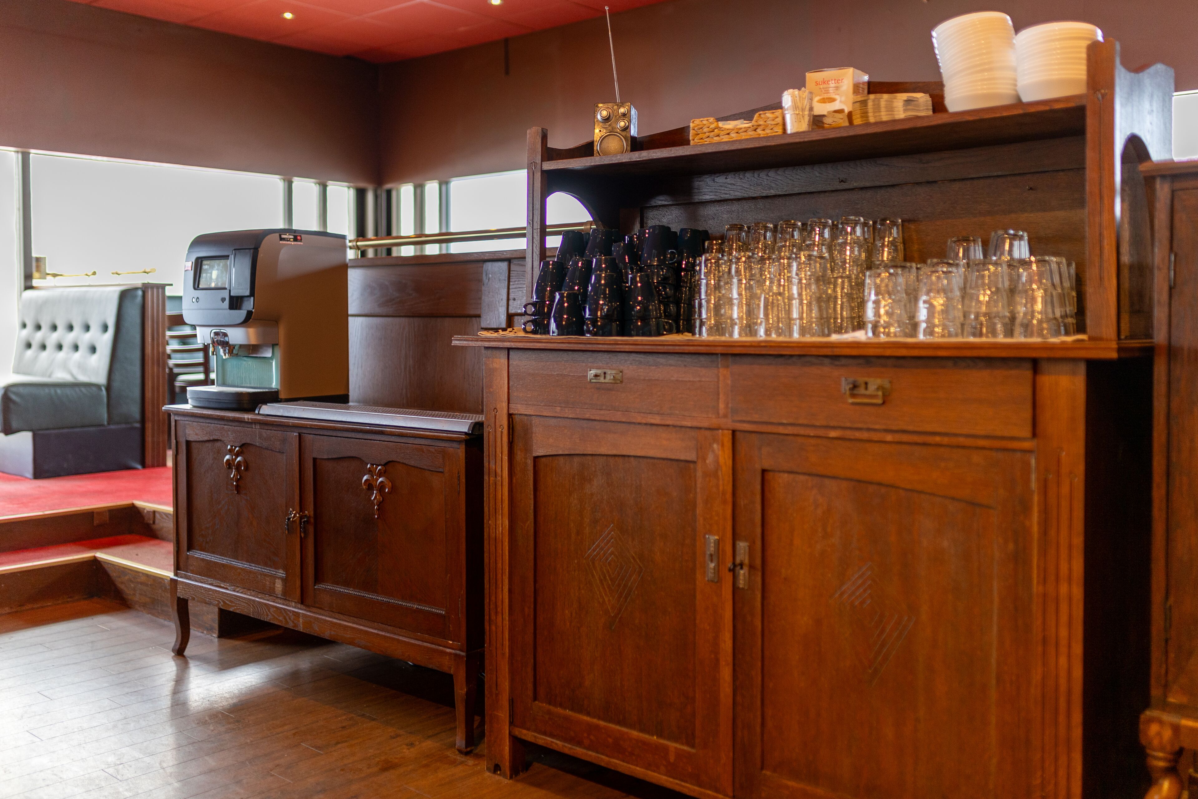 Un coin bar en bois avec une machine à café, des verres empilés et une radio.