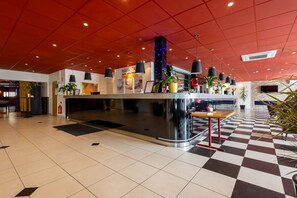 Un hall de hotel con techo rojo, suelo a cuadros y una recepción con plantas en macetas.