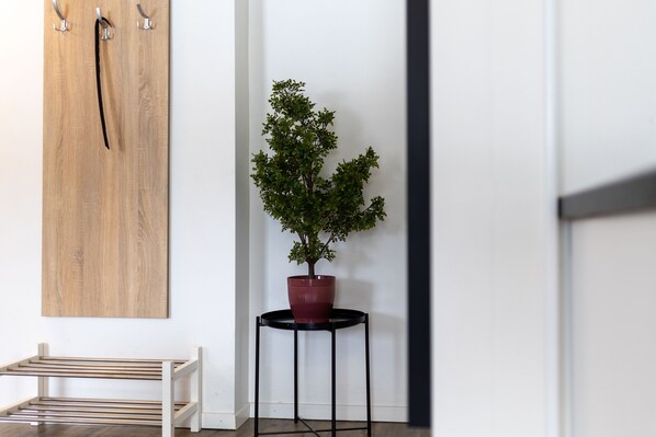 Pared de madera con un perchero colgado, una mesita redonda con planta en maceta y un banco con listones horizontales.