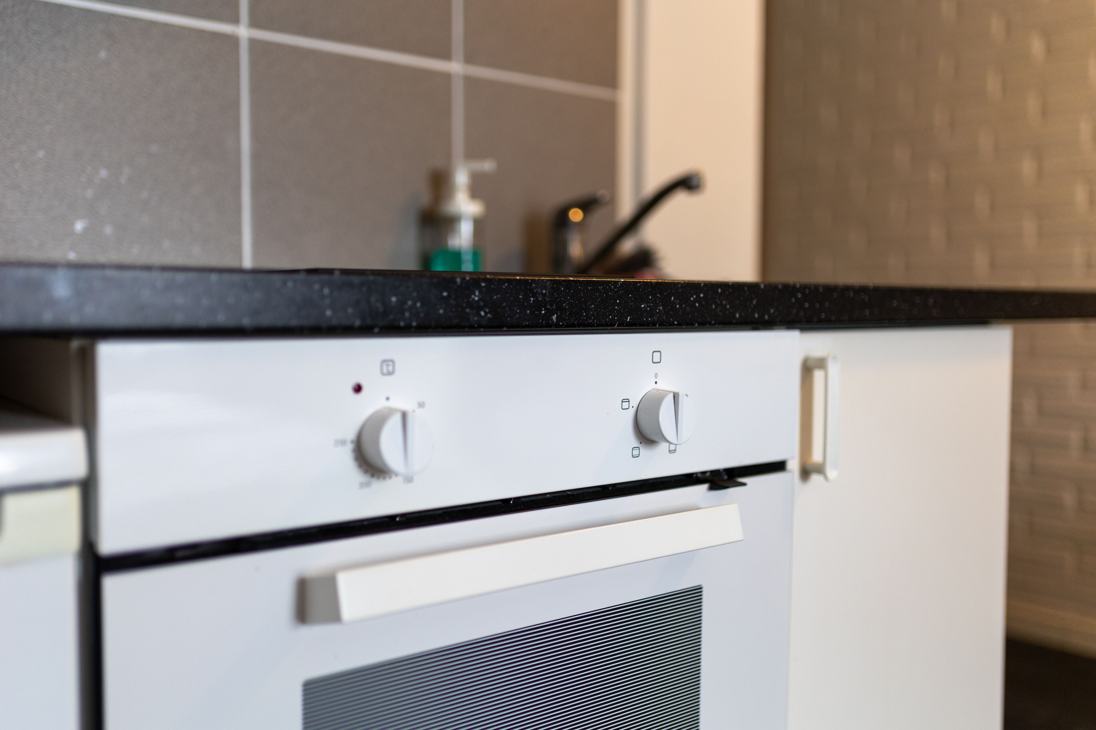 A kitchen with a black countertop, white appliances, and a tiled backsplash.