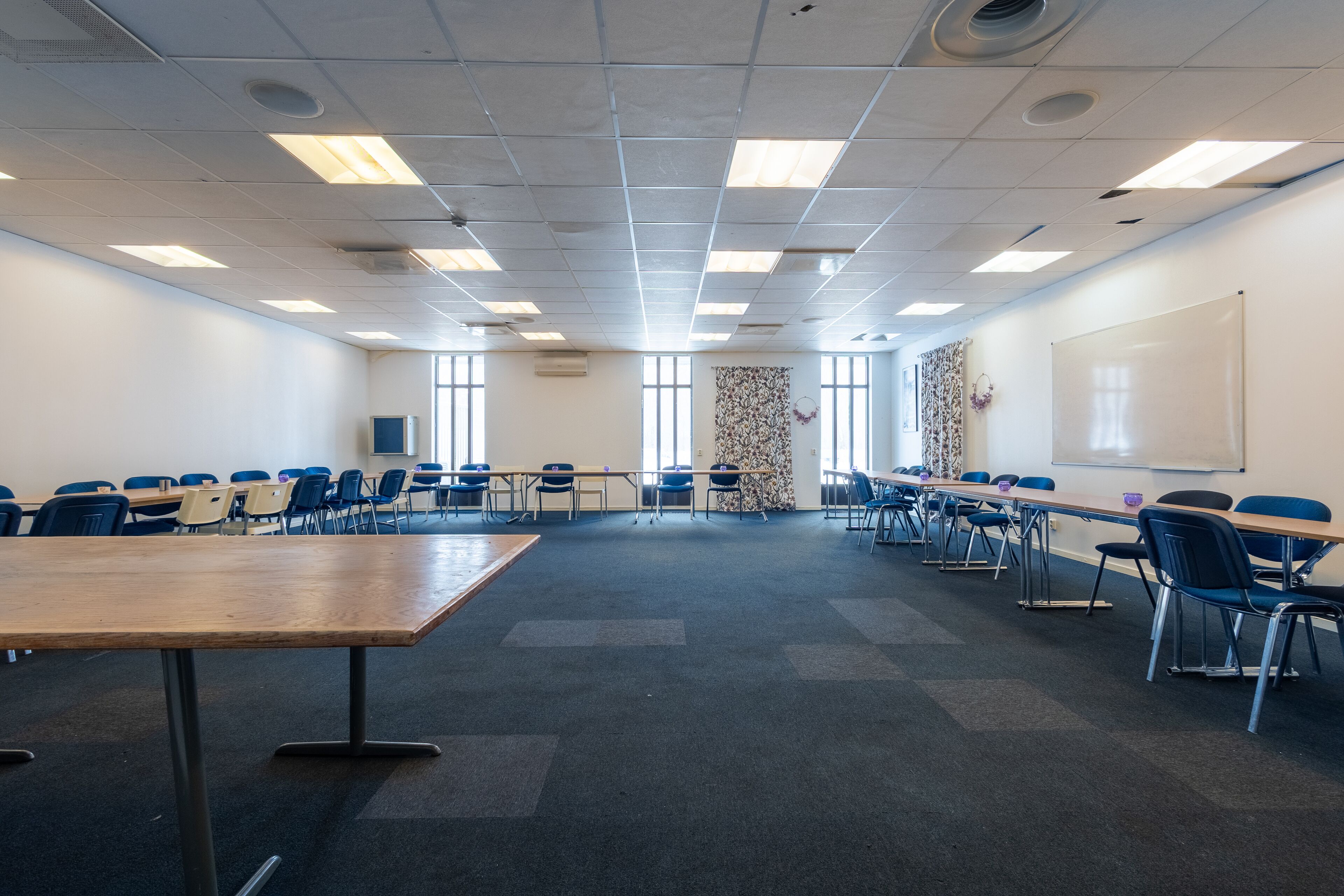 Een vergaderzaal met een lange tafel, stoelen, een whiteboard en een behang met een patroon.