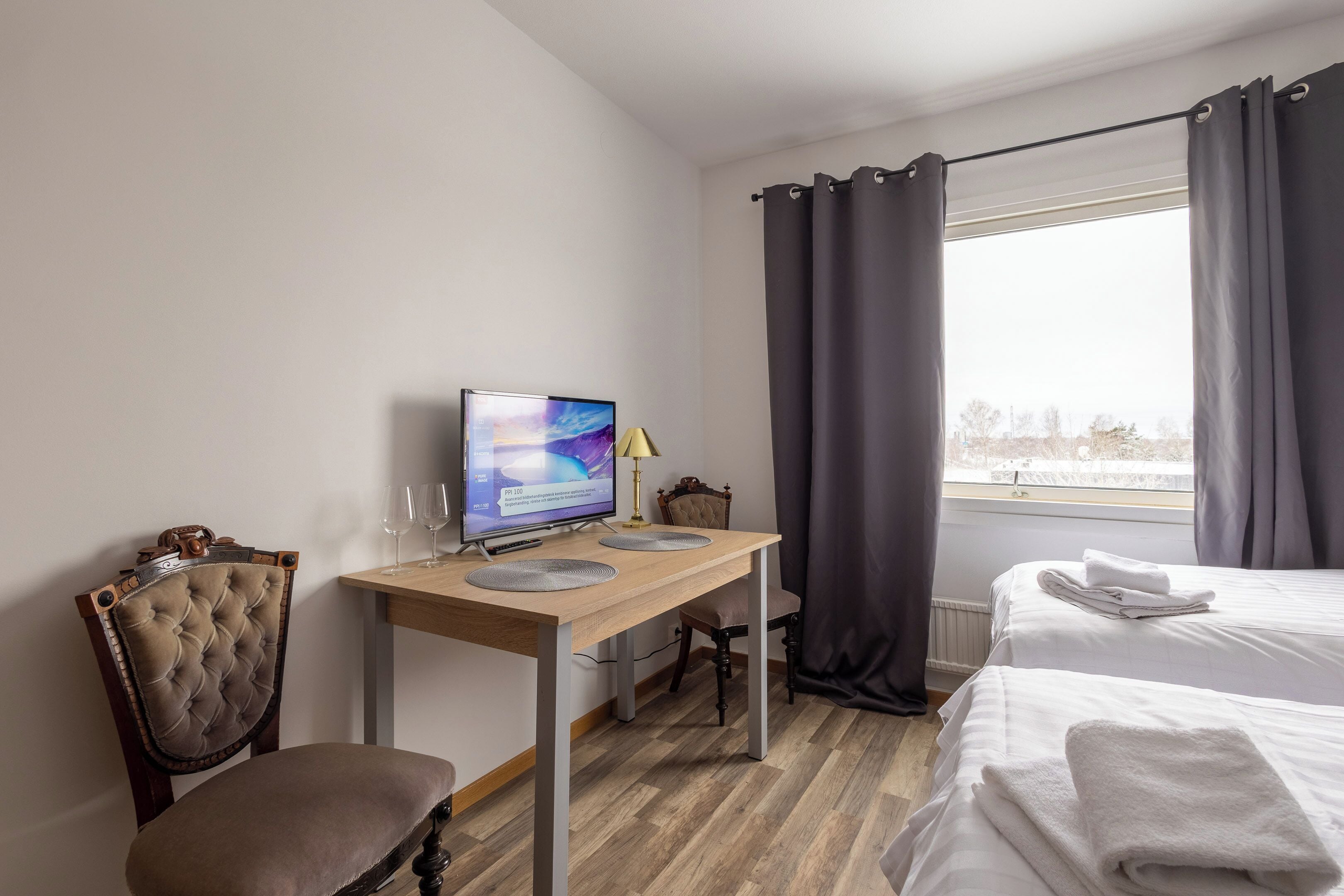 A hotel room with a wooden desk, a computer, a chair, a bed, and a window with curtains.