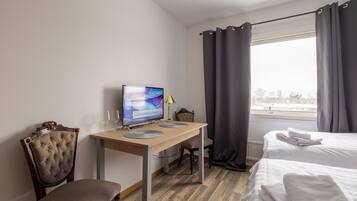 A hotel room with a wooden desk, a computer, a chair, a bed, and a window with curtains.