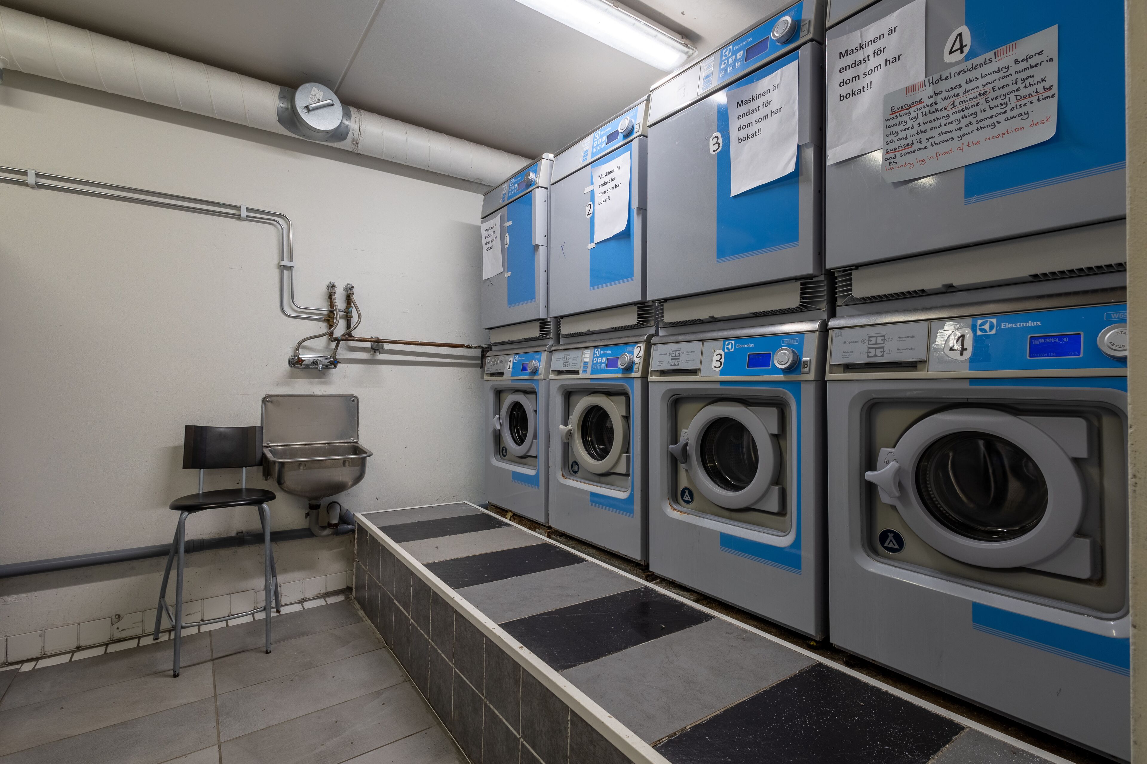 A laundry facility with four washing machines, a sink, and a chair.