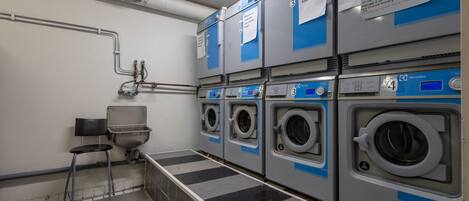 A laundry facility with four washing machines, a sink, and a chair.