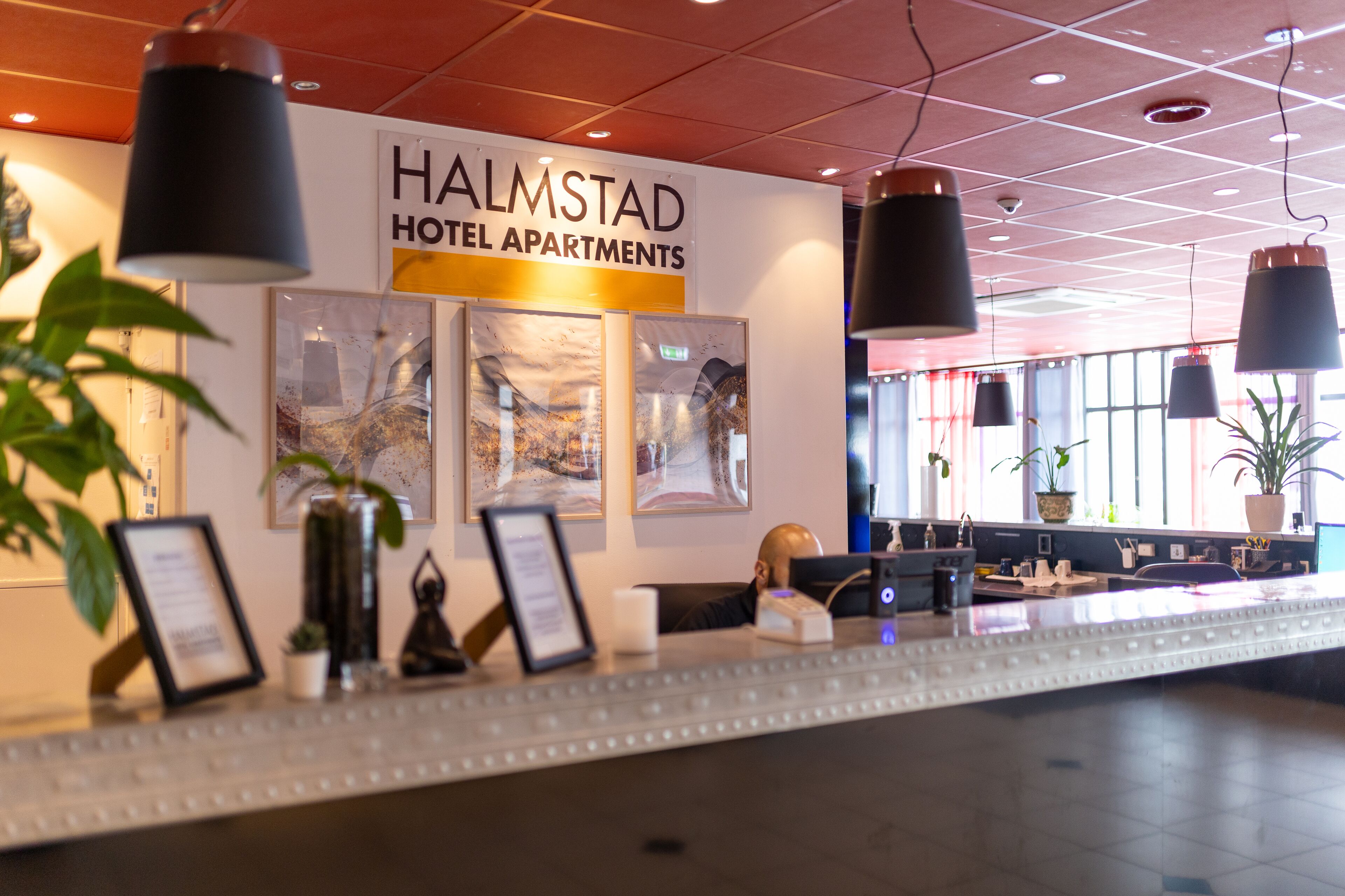 A hotel reception desk with a sign reading "HALMSTAD HOTEL APARTMENTS."