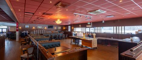 A spacious restaurant with a high ceiling, wooden flooring, and a bar area.
