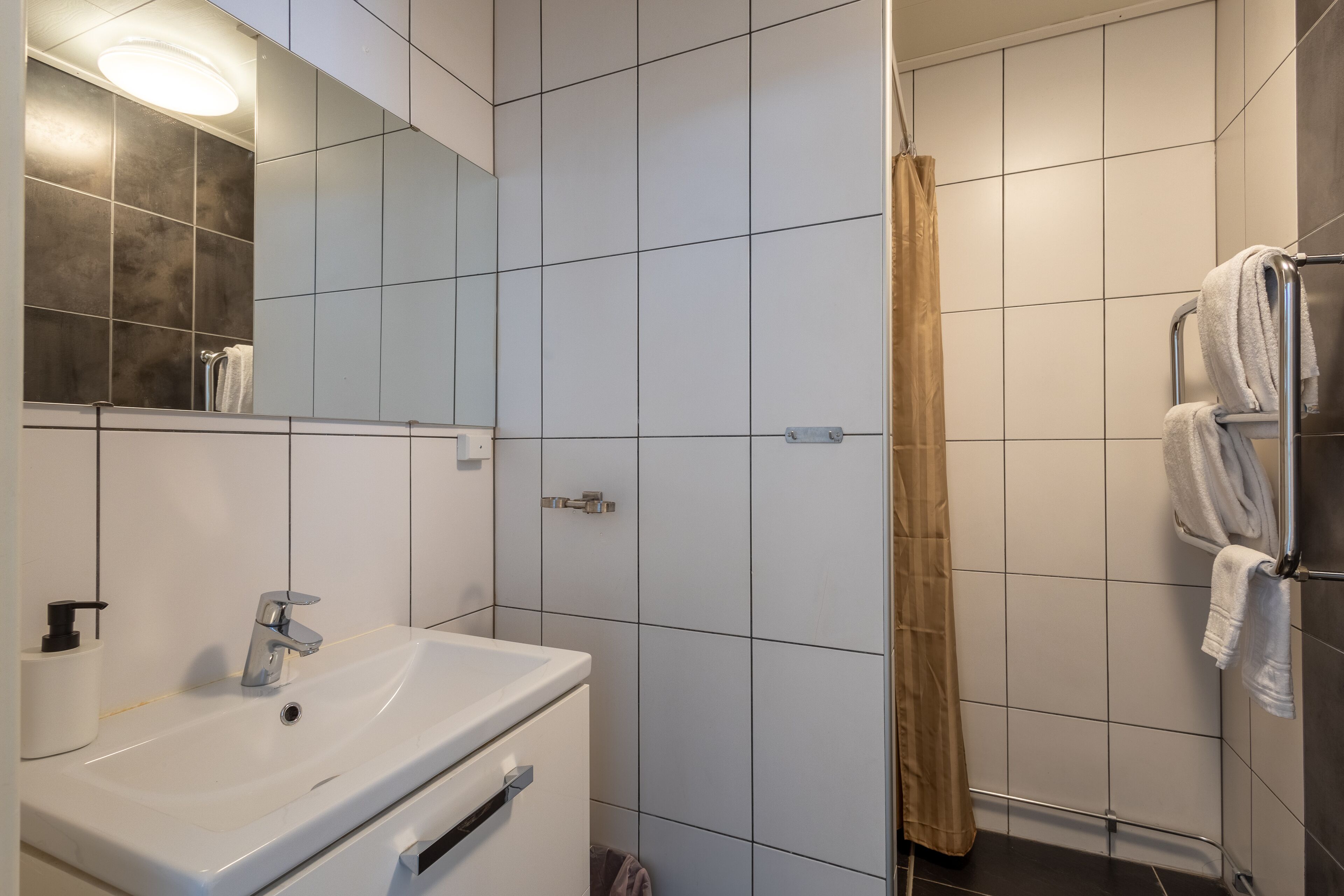 A bathroom with a sink, mirror, and shower area.