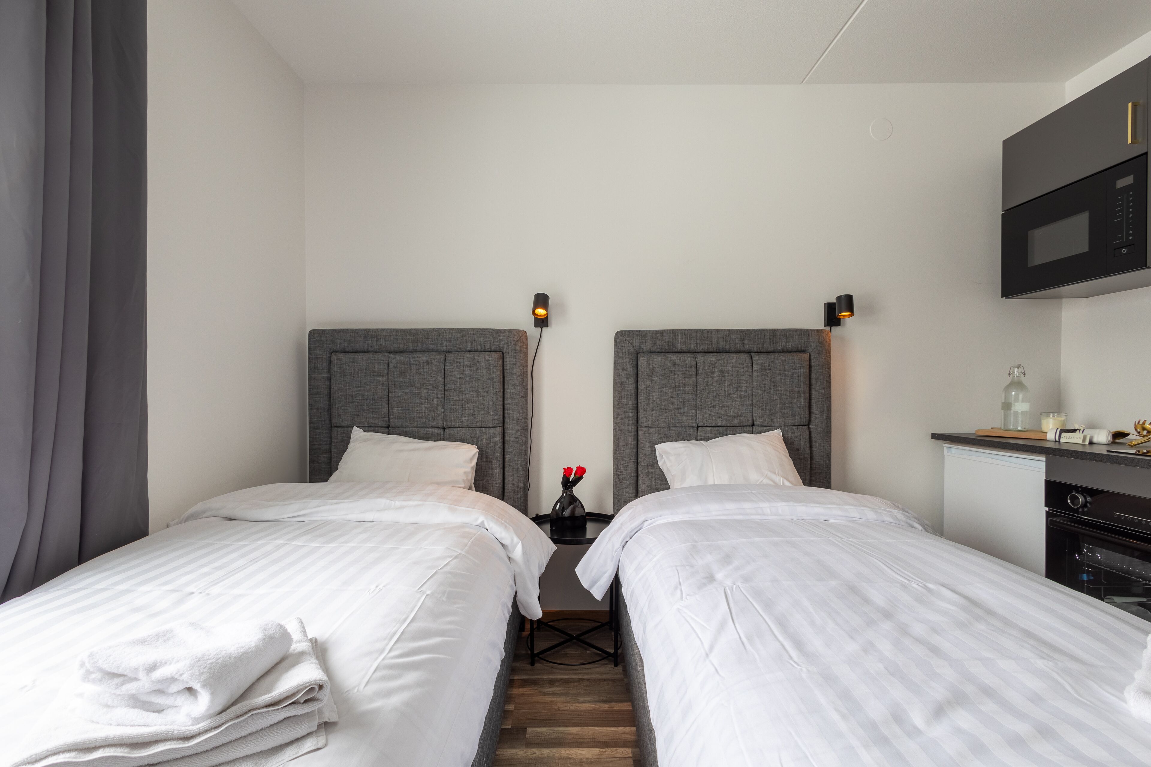 Ein Hotelzimmer mit zwei Einzelbetten, einem kleinen Tisch mit einer Vase voller roter Blumen, einer Mikrowelle und einem kleinen Kühlschrank.