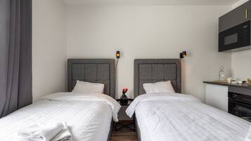 Ein Hotelzimmer mit zwei Einzelbetten, einem kleinen Tisch mit einer Vase voller roter Blumen, einer Mikrowelle und einem kleinen Kühlschrank.