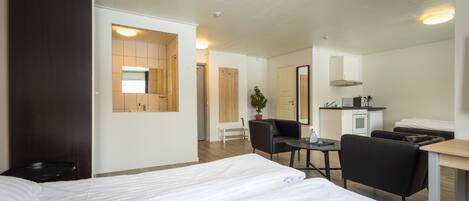 Habitación de hotel con cama, escritorio, silla, pequeña mesa, planta en maceta y kitchenette.