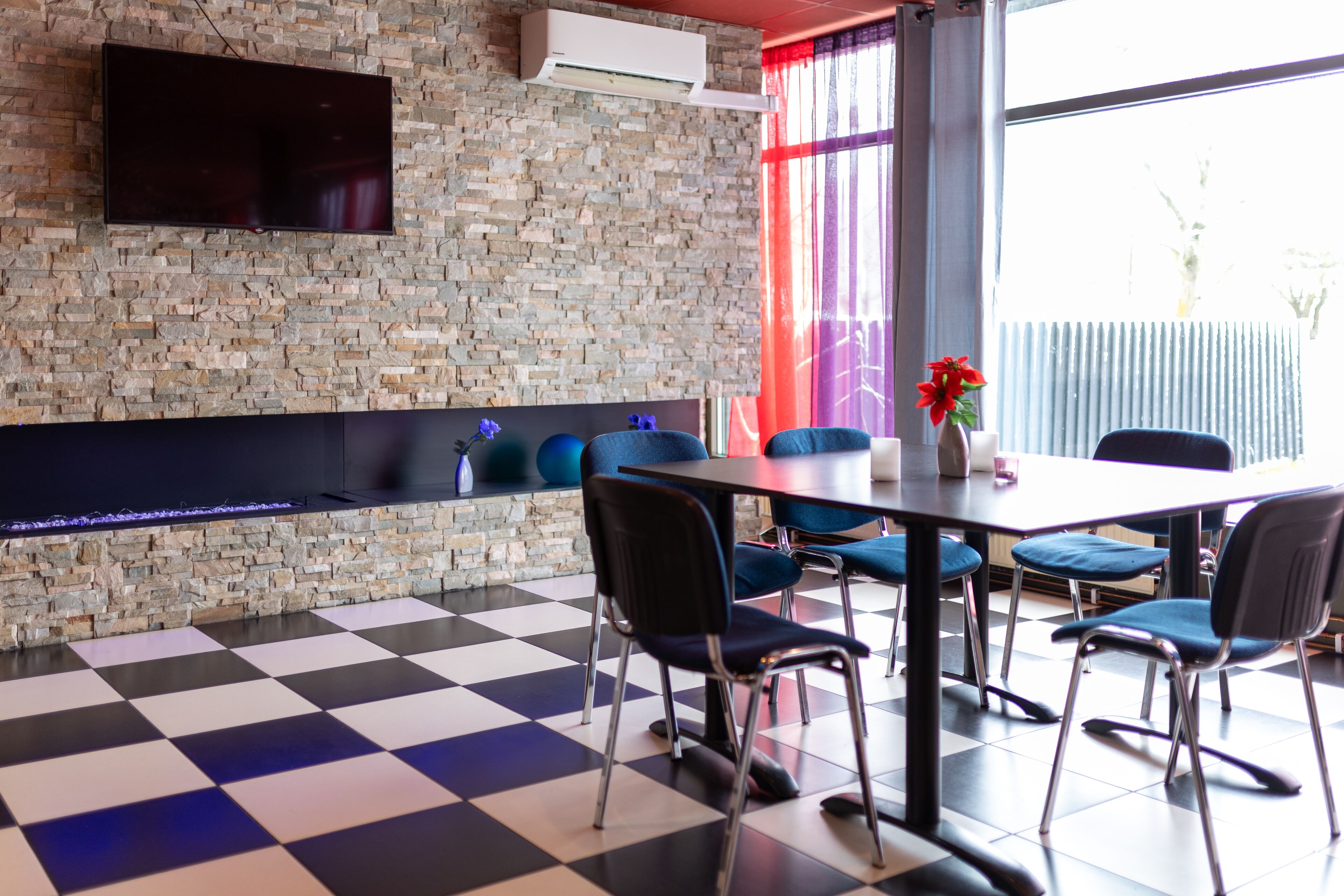 Una habitación moderna con suelo a cuadros, pared de piedra, televisor de pantalla plana y una mesa con sillas.