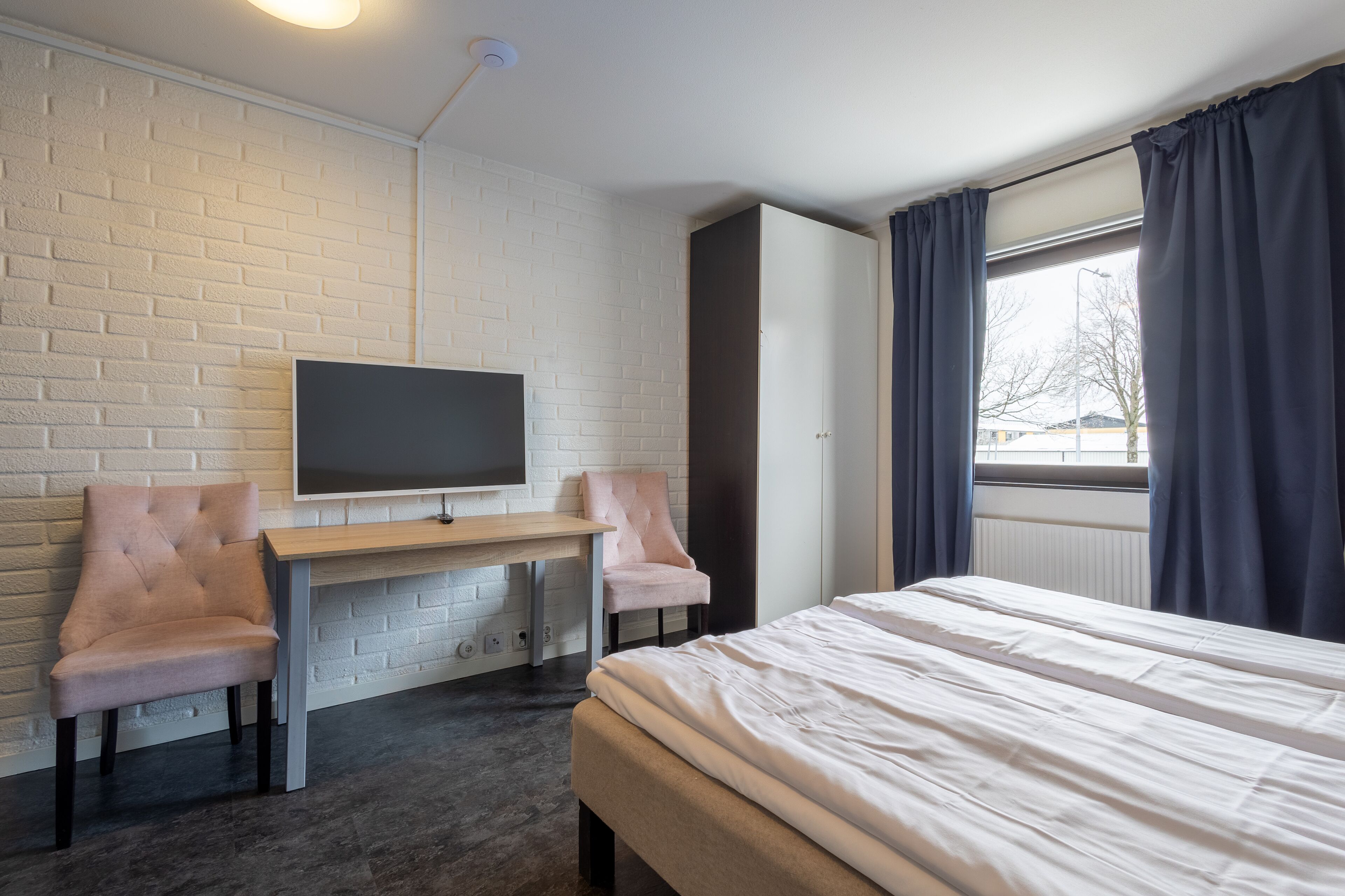 Ein modernes Zimmer mit einem Bett, einem an einer Ziegelwand befestigten Fernseher, einem Schreibtisch und zwei Stühlen.