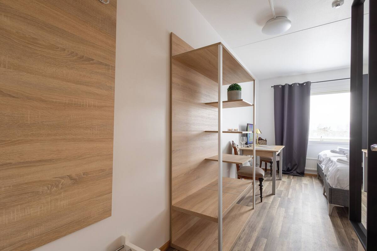 Ein modernes Schlafzimmer mit Holzboden, Schreibtisch mit Stuhl, Bett und großem Spiegel.