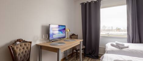 Habitación de hotel con escritorio de madera, computadora, silla, cama y ventana con cortinas.