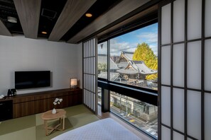 A modern hotel room with a large window, a flat-screen TV, a wooden bedside table, and a traditional Japanese sliding door. - Hotel Crush On (Kyoto)