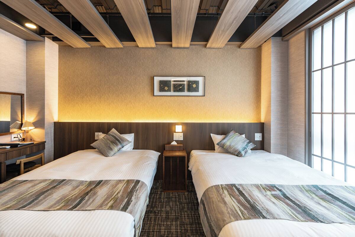A hotel room with two beds, a nightstand, a lamp, and a framed picture on the wall.