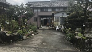 A traditional Japanese building with a tiled roof, surrounded by potted plants and a gravel path leading to the entrance. - A house with a rural garden (魚津市)