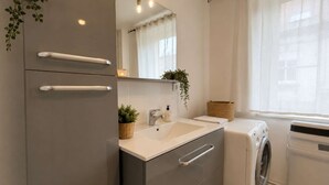 A modern bathroom with a built-in sink, a mirror, a washing machine, and a small plant. - Le Central (Wimereux)