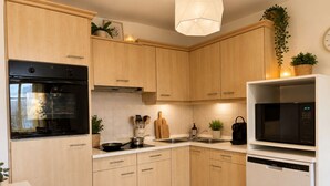 A modern kitchen with wooden cabinets, a black oven, a microwave, and a dishwasher. - Le Central (Wimereux)