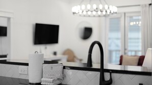 Eine moderne Küche mit schwarzem Arbeitsplatz, weiß gefliestem Rückspritzschutz, einem schwarzen Wasserhahn, einem Handtuchspender und einem an der Wand montierten Flachbildfernseher.