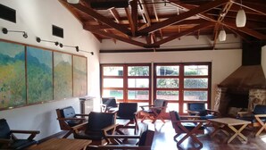 A rustic interior with wooden furniture, large windows, and a stone fireplace. - Kuntur Posada (Capilla del Monte)