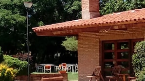 A brick building with a tiled roof, a chimney, and a patio area with chairs and tables. - Kuntur Posada (Capilla del Monte)