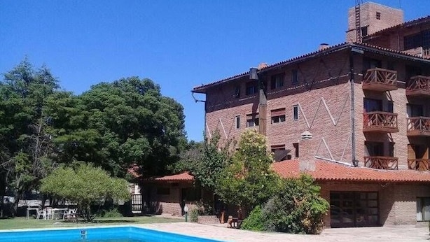 A pool area with a clear blue pool, surrounded by a building with multiple balconies and a brick facade. - Kuntur Posada (Capilla del Monte)