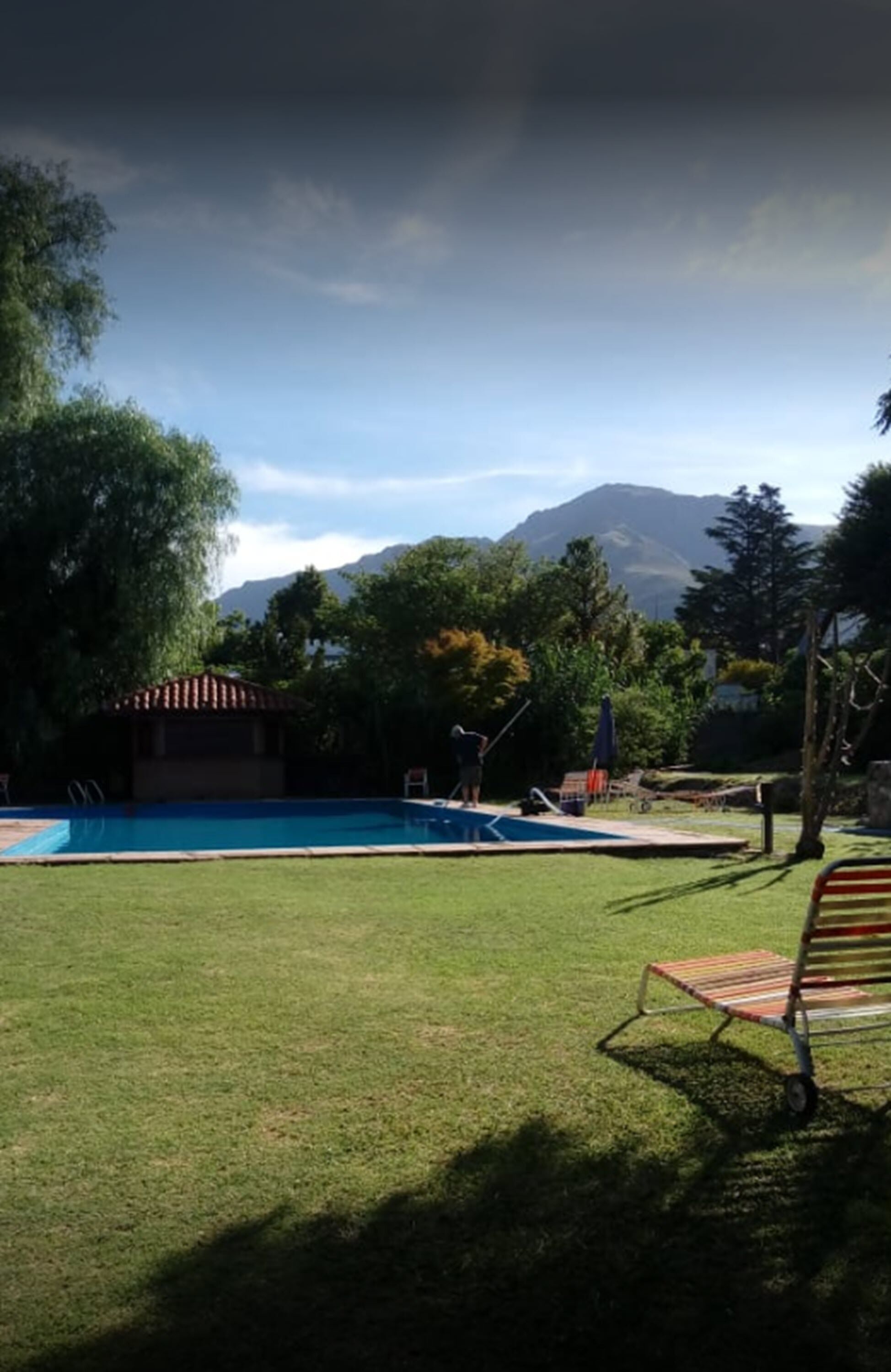 A swimming pool with a grassy area, a small building, and trees.