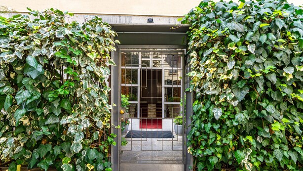 A building entrance with a metal gate, a red mat, and a concrete pathway leading to a door. - 2 Bedrooms Apartment in the City Center (Milan)