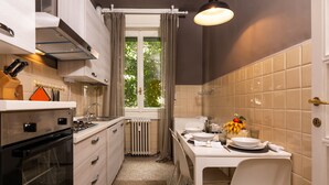 A compact kitchen with a stove, oven, and a dining area with a table set for two. - 2 Bedrooms Apartment in the City Center (Milan)