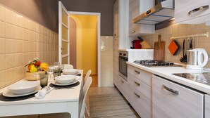 A modern kitchen with white cabinets, a gas stove, and a coffee maker. There is a dining table set with plates, glasses, and a fruit bowl. - 2 Bedrooms Apartment in the City Center (Milan)
