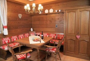 A wooden dining room with a central table, heart-patterned cushions, and a chandelier. - Rustic apartment in the Dolomites (Abfaltersbach)