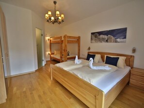 A bedroom with a large bed, a bunk bed, wooden flooring, a chandelier, and a painting on the wall. - Rustic apartment in the Dolomites (Abfaltersbach)