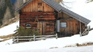 Una cabaña de madera rústica con techo inclinado, rodeada de nieve y con montañas nevadas al fondo.