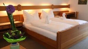 A neatly made bed with white linens and pillows, a wooden headboard, and a bedside table with a lamp.