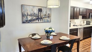 A dining area with a wooden table set for four, a vase with flowers, and a painting of a bridge on the wall. - Awesome Condo in Central Raleigh (Raleigh)