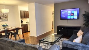 A modern living room with a grey sofa, a glass coffee table, and a flat-screen TV mounted on the wall. - Awesome Condo in Central Raleigh (Raleigh)